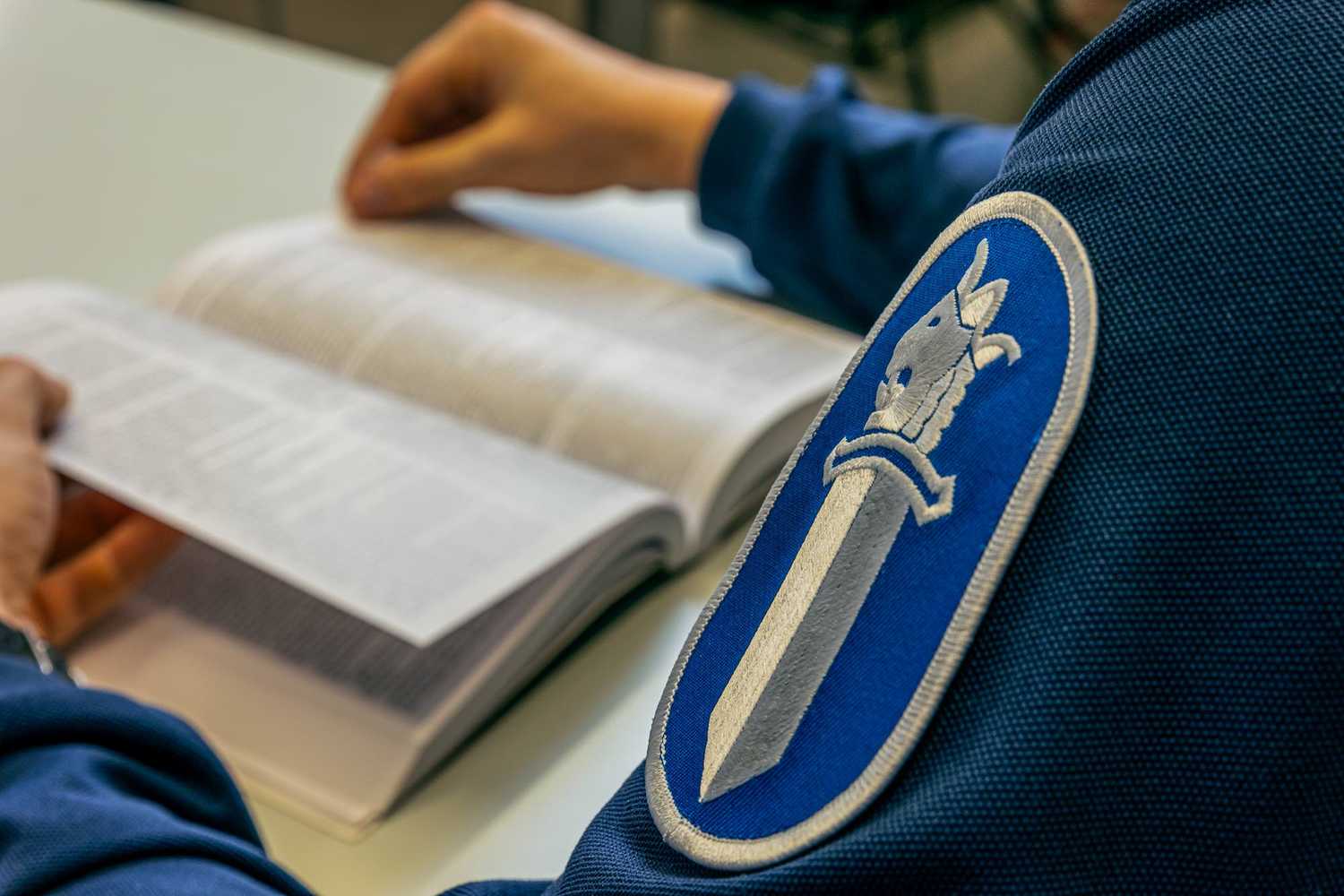 A police officer is reading a law book. Police sleeve badge with sword logo in the foreground.