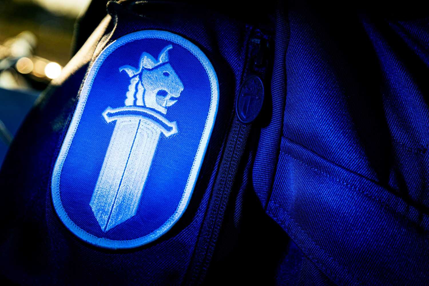Poliisin sinivalkoinen miekkalogo sinisen kenttähaalarin hihassa.